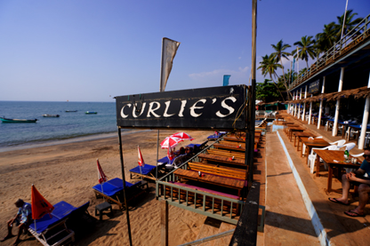 Curlies Beach Bar on Anjuna Beach in North Goa. Blue sunbeds with beach brollies stretch along the beach in front of the dining tables.