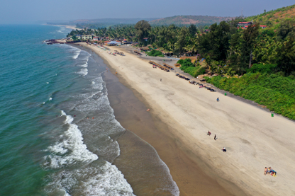 View of Ashwen Beach India with the ocean to the left, beach running diaganally from the bottom right hand corner and the green hills of Goa behind.