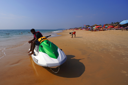 Man sitting on a jet ski parked on Calangute Beach in North Goa India with the ocean to the left, the beach behind and to the right with beach bars and beach shacks in the background.