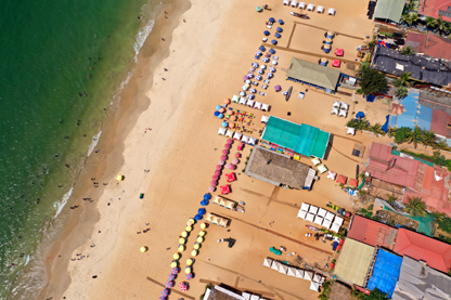Top down view of Baga Beach in north Goa showing beach shacks and beach umbrellas along the beach with the ocean to the left